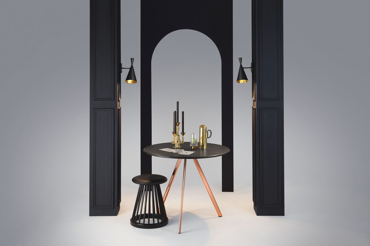 Schwarze Tom Dixon Beat Wandleuchte als stilvolle Innenraumbeleuchtung über einem Tisch mit Dekoration.