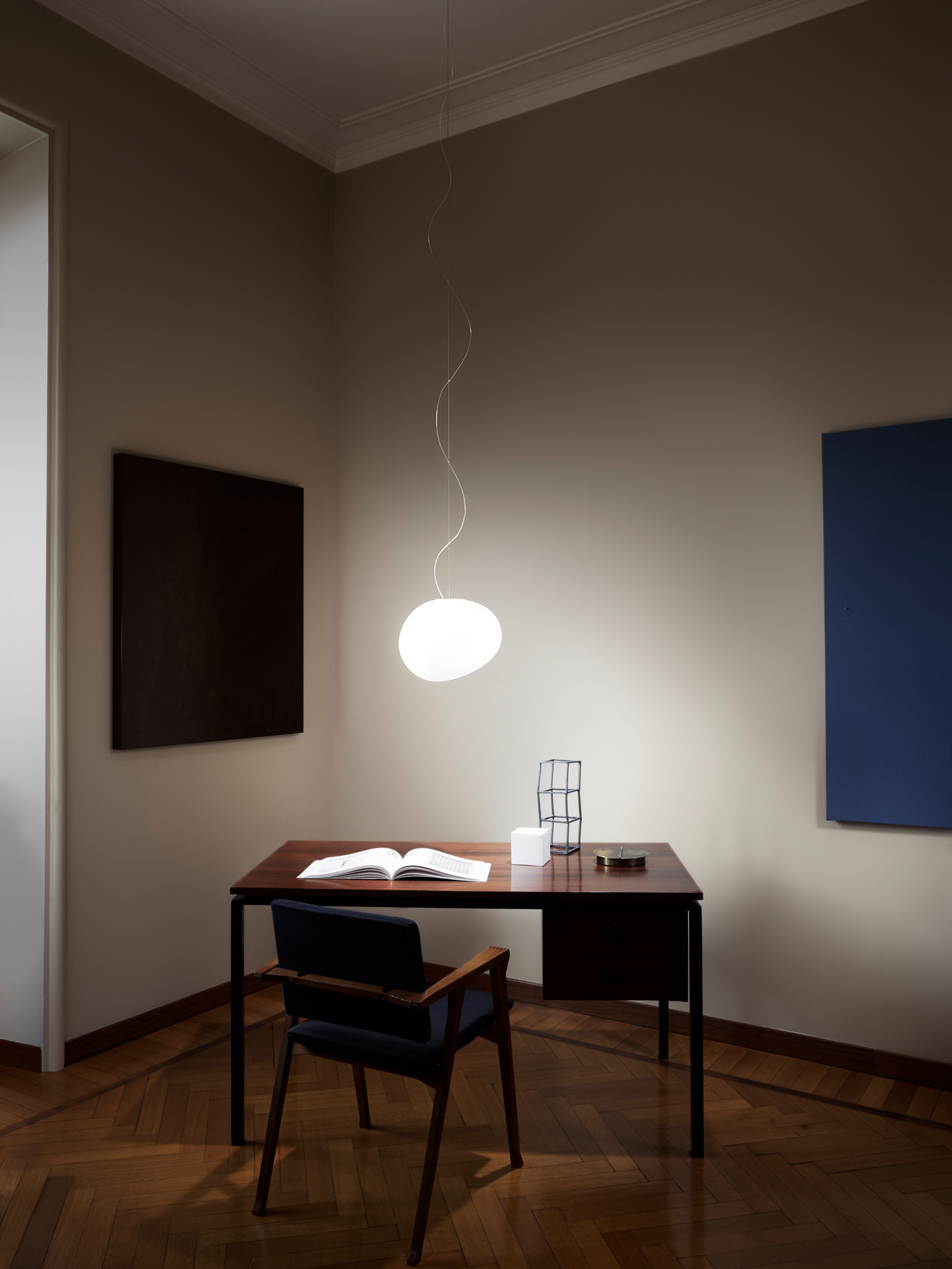 Gregg Pendelleuchte von Foscarini über einem dunklen Schreibtisch in einem stilvollen Arbeitszimmer mit Kunst.
