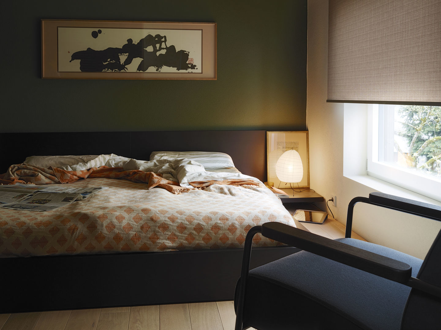 Schlafzimmer mit Bett, Nachttischlampe und einem Vitra Fauteuil Direction Sessel im Vordergrund, der zum Entspannen einlädt.