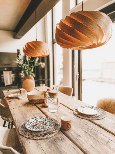 Esstisch aus Holz mit Geschirr und zwei modernen Holz-Pendelleuchten im skandinavischen Stil.