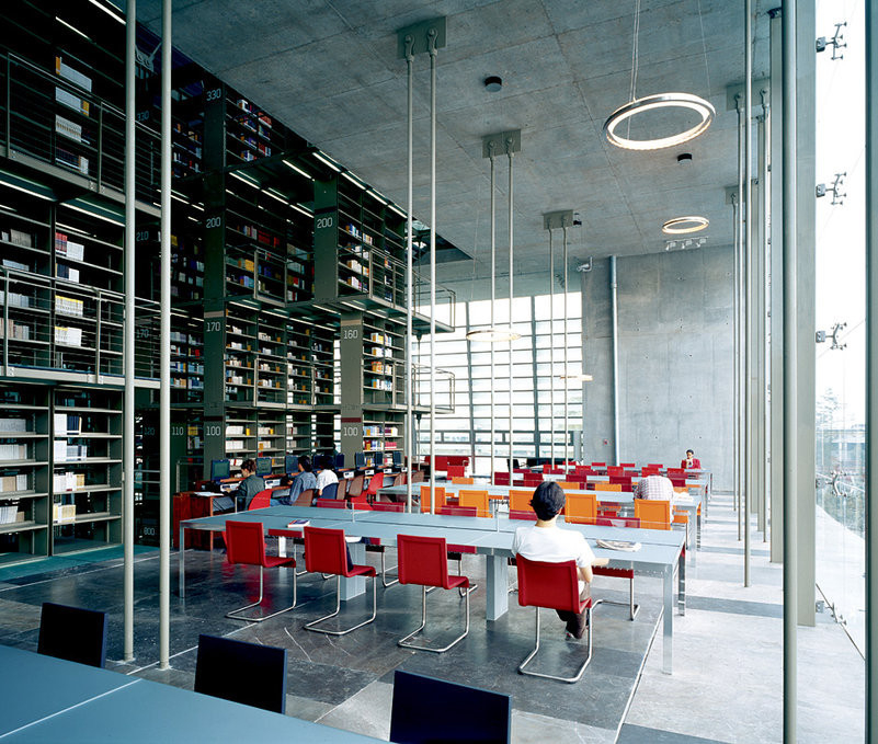 Innenaufnahme einer Bibliothek mit roten Vitra .05 Stühlen an langen Tischen unter Regalen.