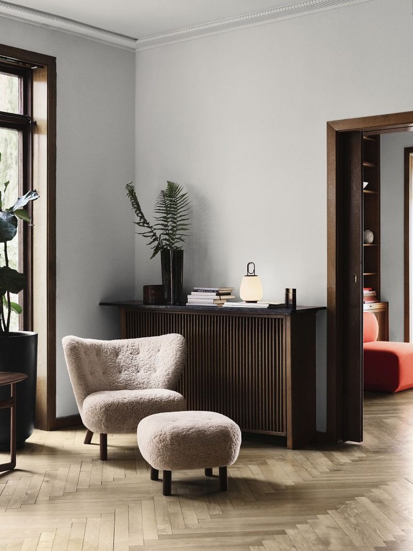 Beige Sessel mit Hocker aus Teddyfell vor dunklem Holzschrank in einem stilvollen Wohnzimmer.