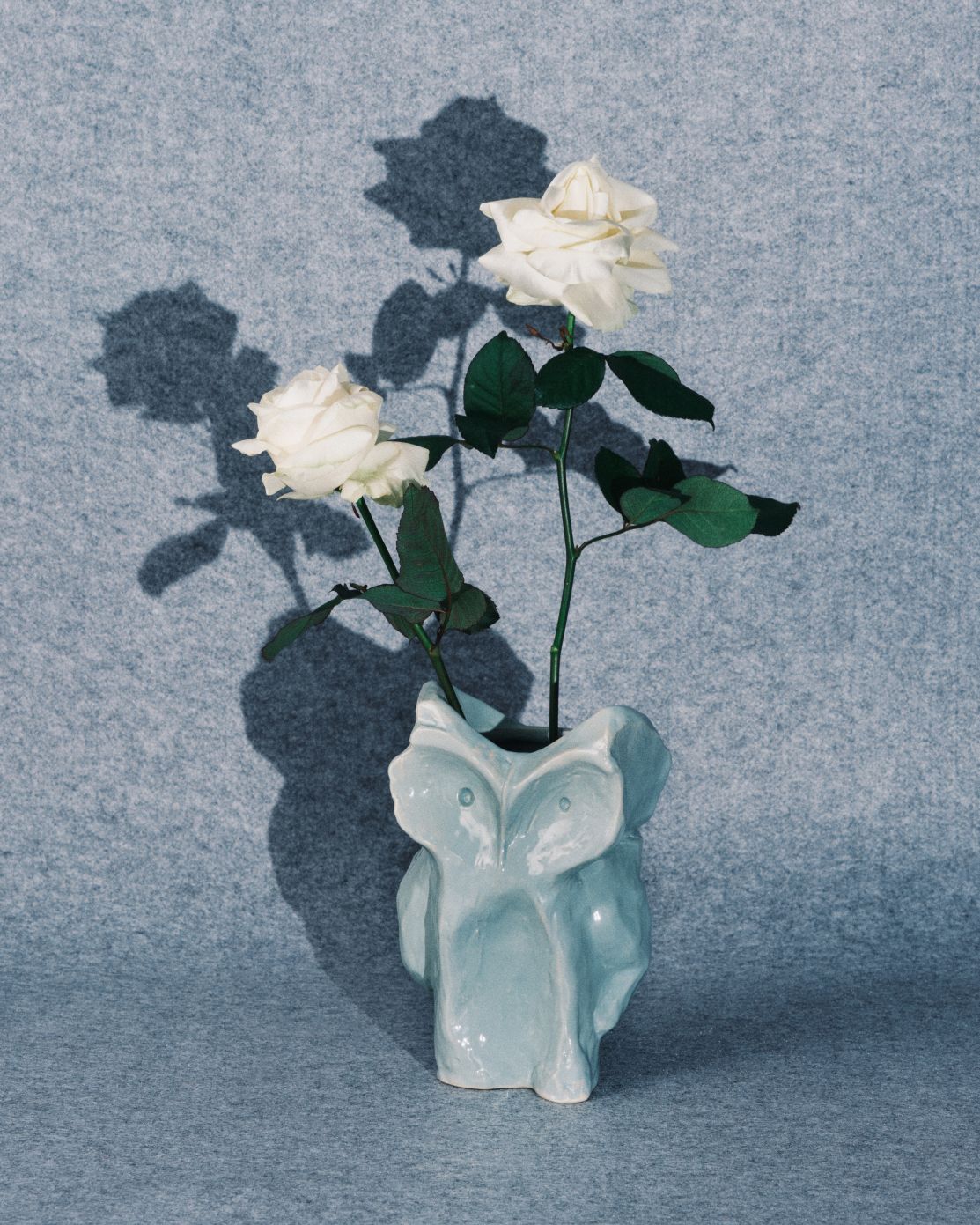 Nahaufnahme der Serax Eule Vase in Aubergine mit weißen Rosen, dekorative Keramik Blumenvase.