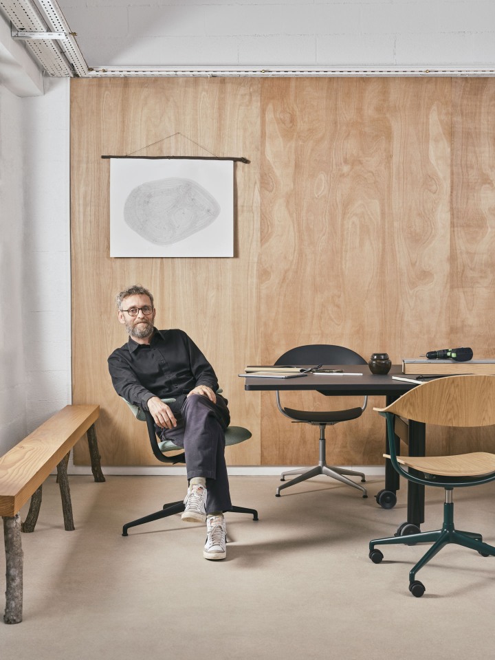 Mann sitzt auf einem Mynt Bürodrehstuhl von Vitra mit Kunststoffschale in einem modernen Büro.