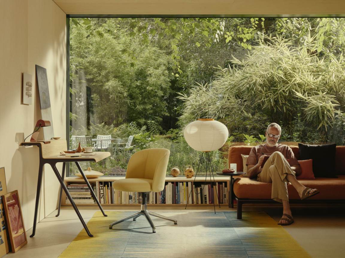 Heller Raum mit Vitra Courier Schreibtisch, gelbem Bürostuhl und Mann auf Sofa vor Fenster.