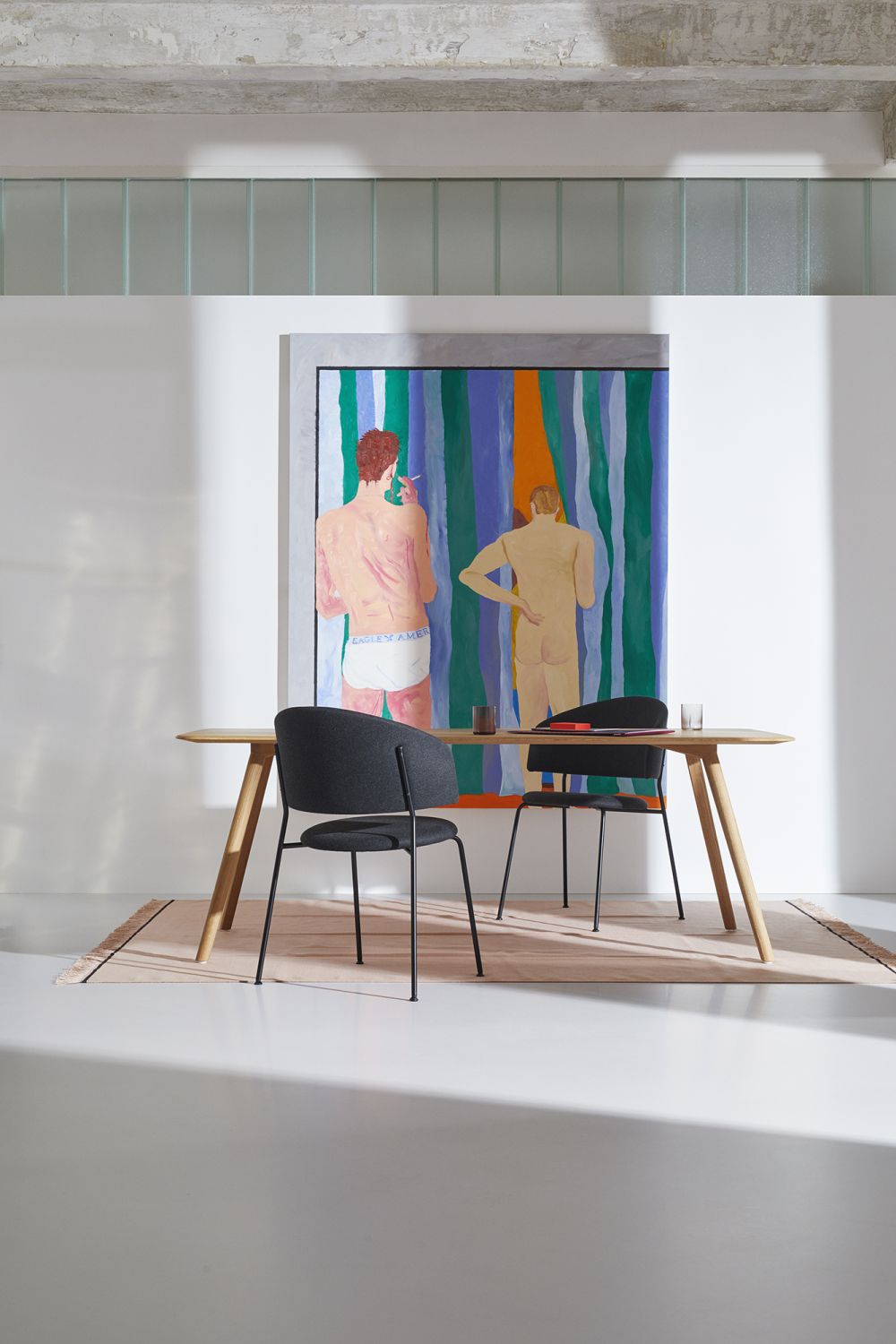 MEYER Tisch Large OUT aus Holz mit zwei Stühlen und abstraktem Gemälde im Hintergrund.