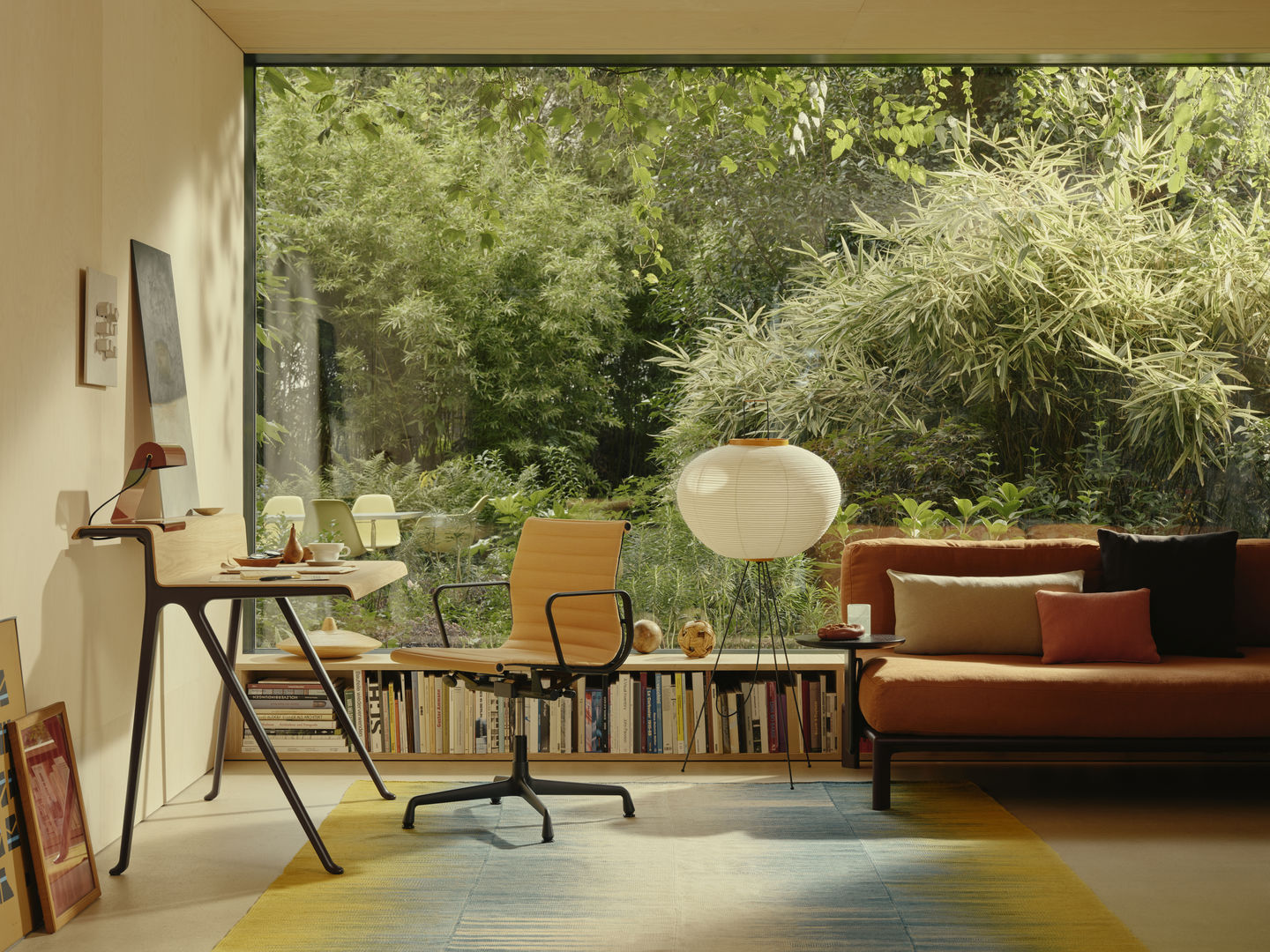 Heller Raum mit Vitra Aluminium Chair EA 131, Schreibtisch und Sofa vor großem Fenster mit Gartenblick.