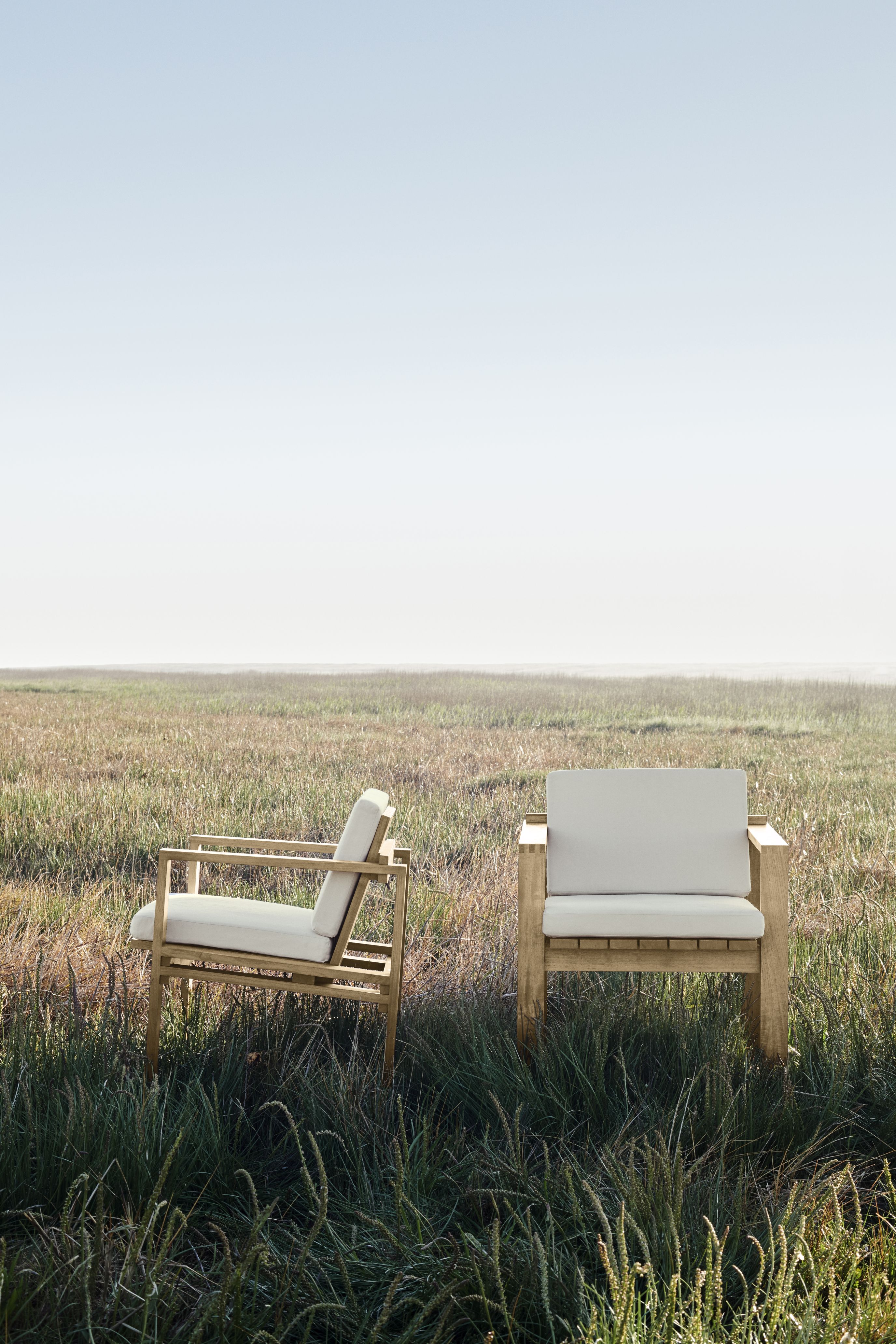 Zwei Bodil Kjaer Sessel Outdoor von Carl Hansen & Søn aus Teakholz mit weißen Polstern im Gras.
