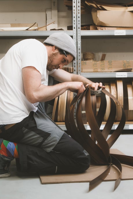 Handwerker fertigt eine moderne Holzlampe aus gebogenen Holzstreifen in einer Werkstatt. Nachhaltige Beleuchtung.