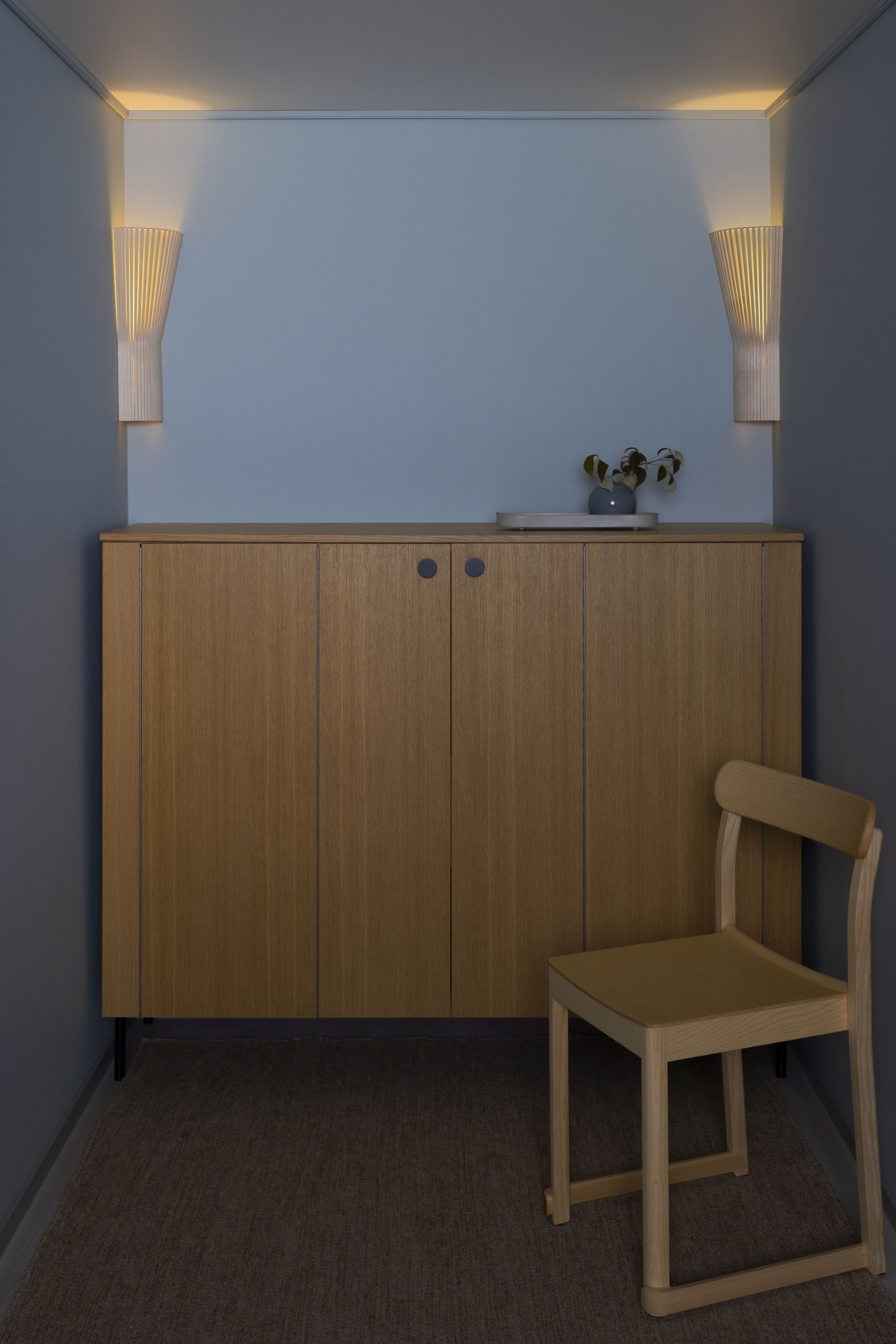 Secto Design 4237 Eckleuchte aus Birkenholz, montiert in einer Ecke über einem Holzschrank mit Stuhl.
