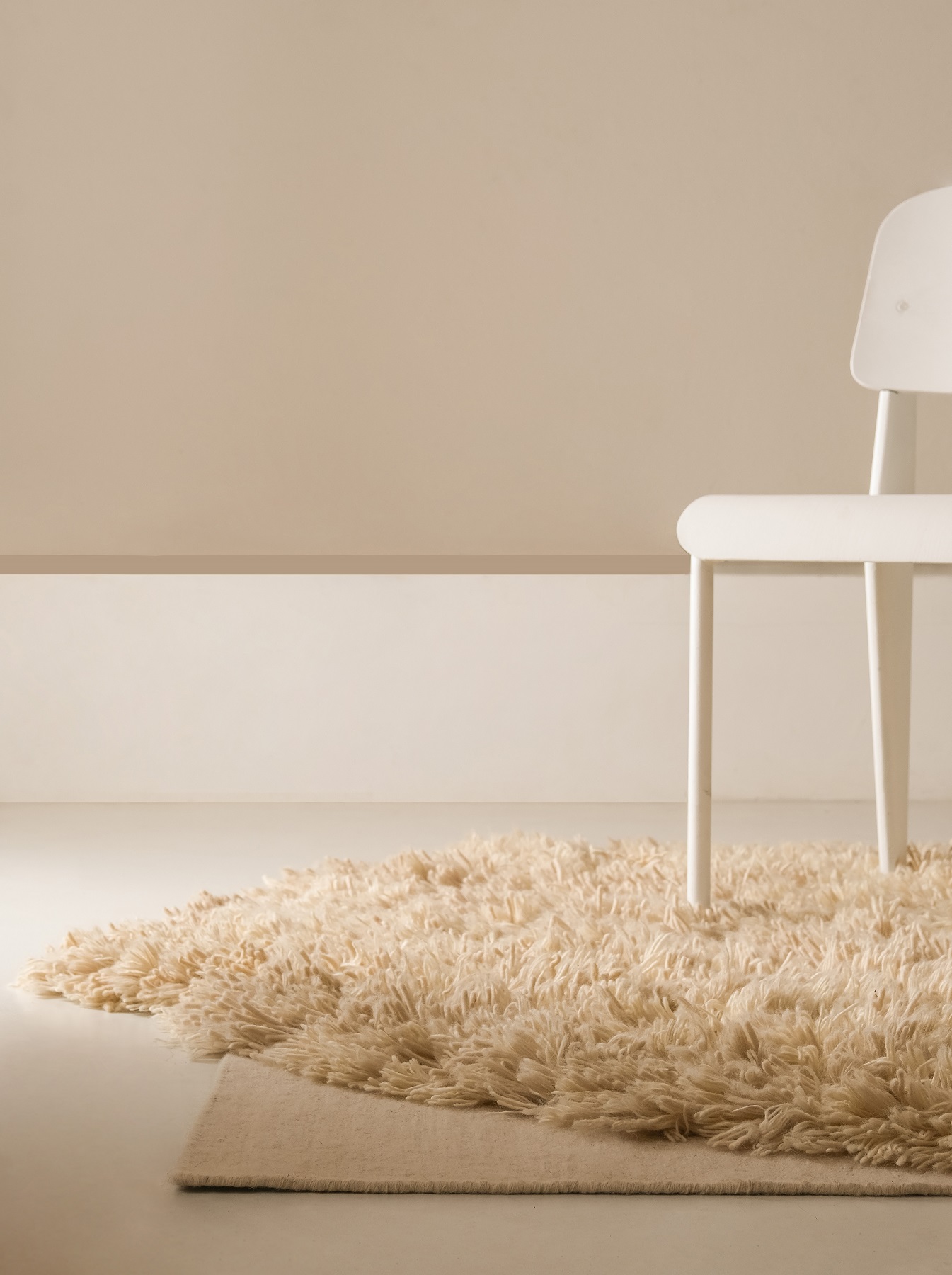 Detailansicht: Beige Alga Teppich von Nanimarquina mit weißem Stuhl auf hellem Untergrund. Hochfloriger Teppich.