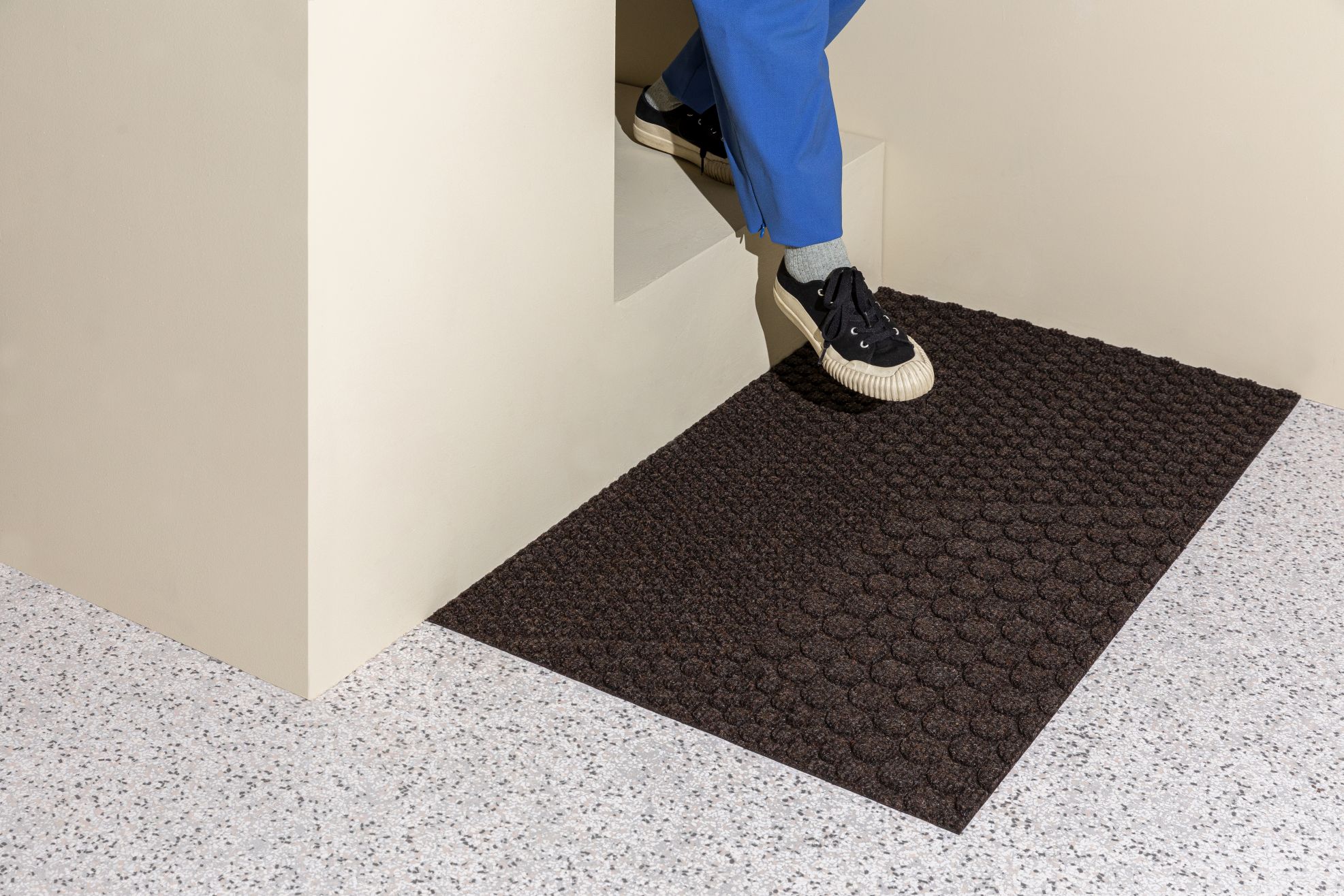Person betritt Haus auf Hex Fußmatte Soil von Heymat, braune Schmutzfangmatte für den Innenbereich.