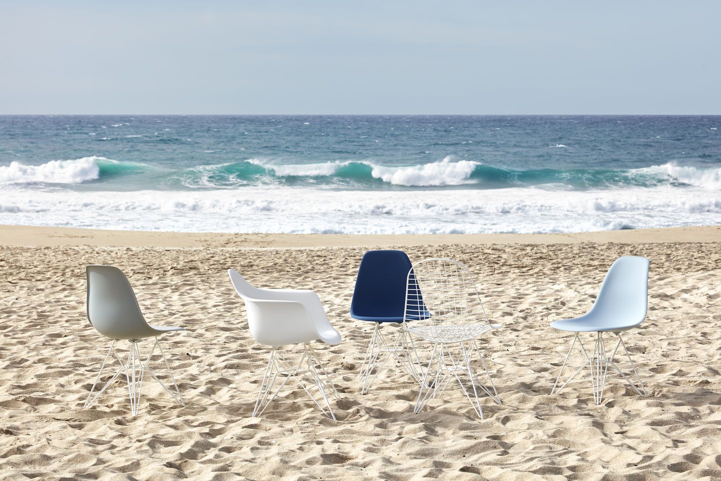 Vitra Eames DSR Stühle aus Fiberglas in verschiedenen Farben am Strand mit Meer im Hintergrund.