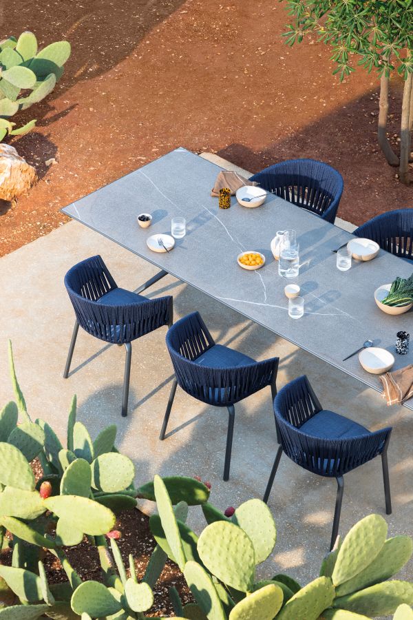 Esstisch-Set für den Außenbereich: Grauer Tisch mit blauen Stühlen und Speisen im mediterranen Garten.