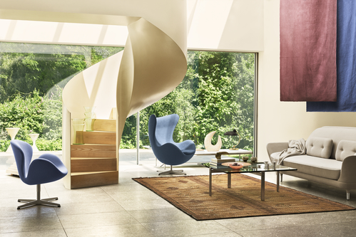 Helles Wohnzimmer mit blauen Sessel-Klassikern, Sofa, Teppich und Wendeltreppe vor Fenster mit Gartenblick.