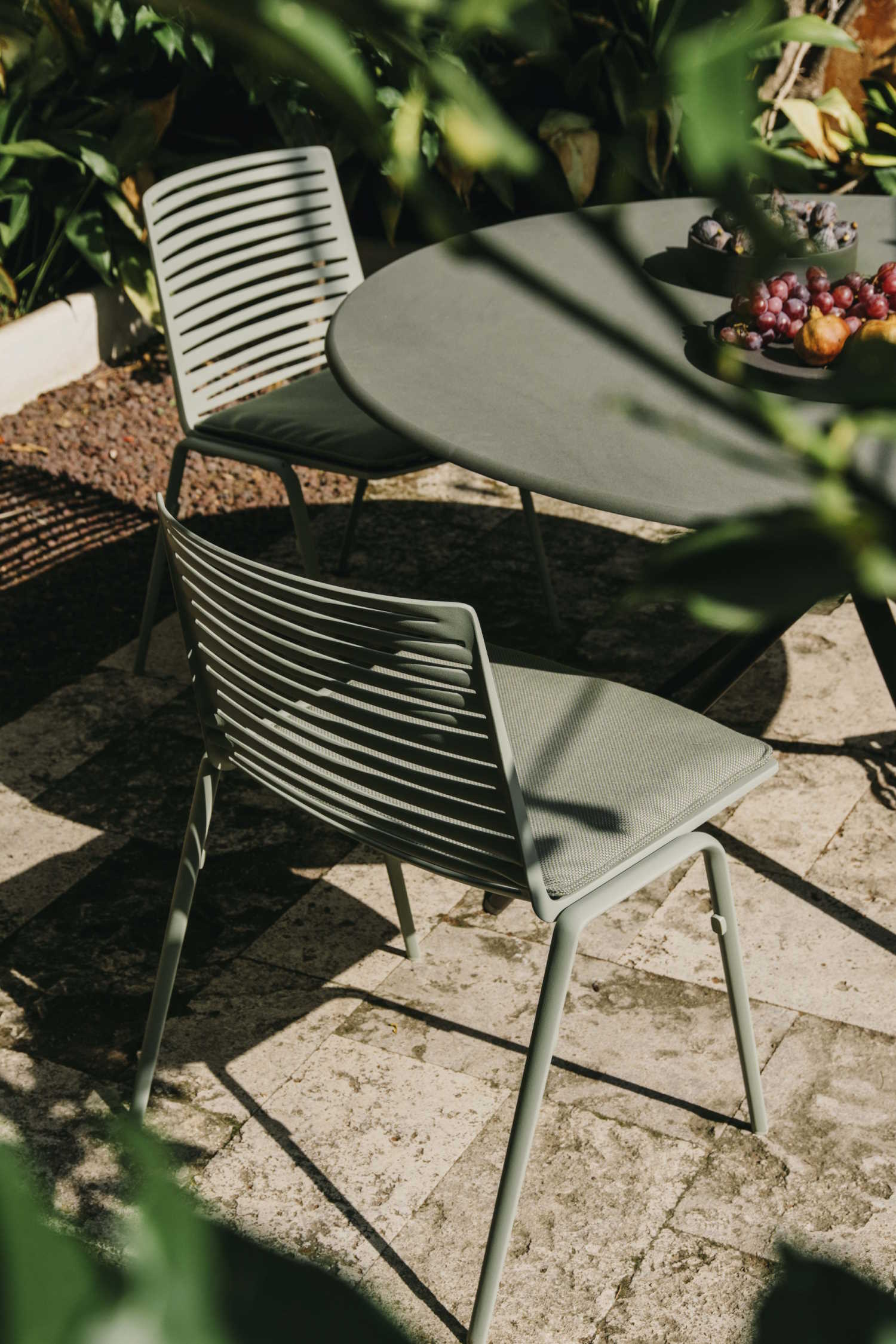 Nahaufnahme von zwei modernen, olivgrünen Gartenstühlen und einem runden Gartentisch mit Obst.