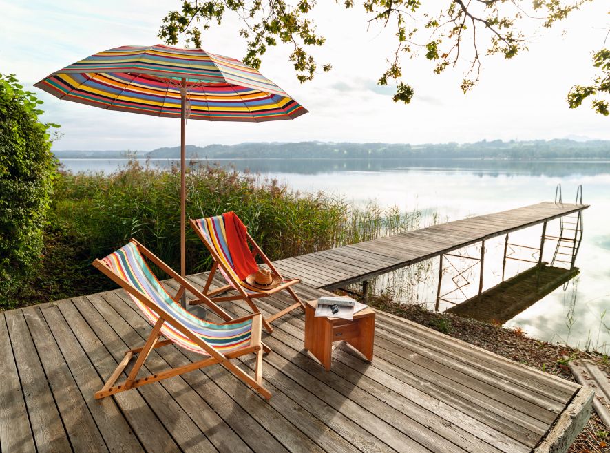 Weishäupl Cabin Liegestuhl auf Holzdeck am See mit Sonnenschirm und Steg. Outdoor Möbel.