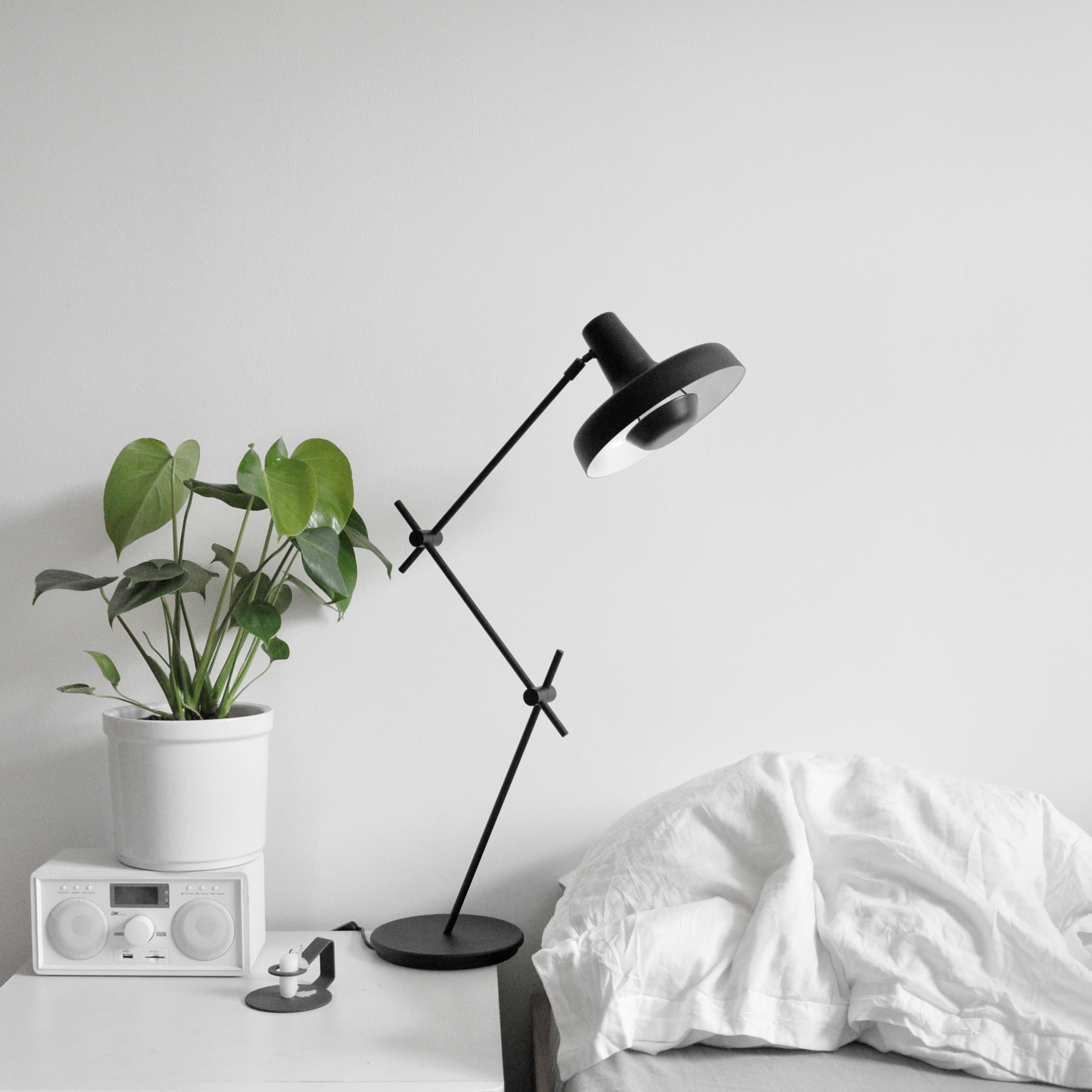 Schwarze Arigato Tischleuchte von Grupa auf Nachttisch mit Pflanze und Radio, modernes Design.