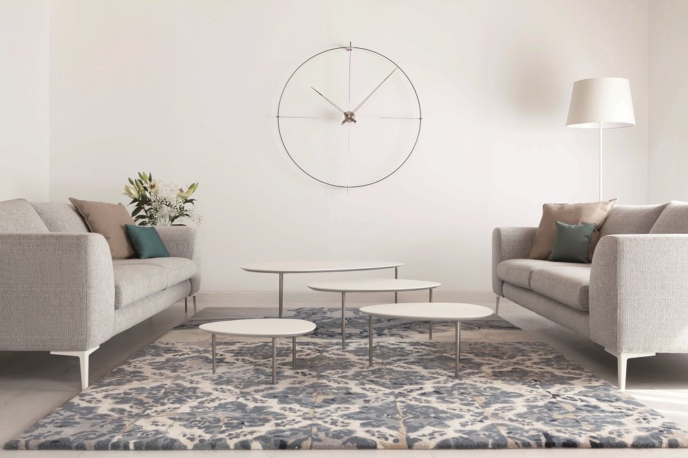 Helle Wohnzimmer-Szene mit Bilbao Nomon Wanduhr, grauen Sofas, Couchtischen und gemustertem Teppich für modernes Interieur.
