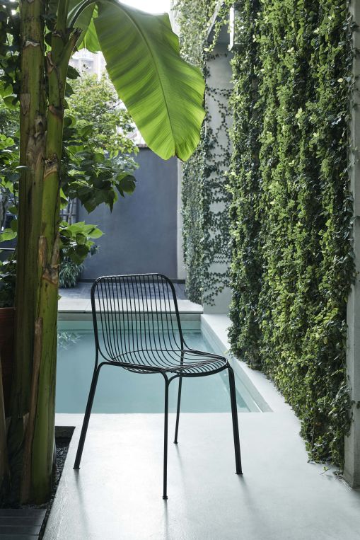 Schwarzer Hiray Outdoor Stuhl mit Armlehne von Kartell, minimalistisches Design, vor Pool und grüner Wand.