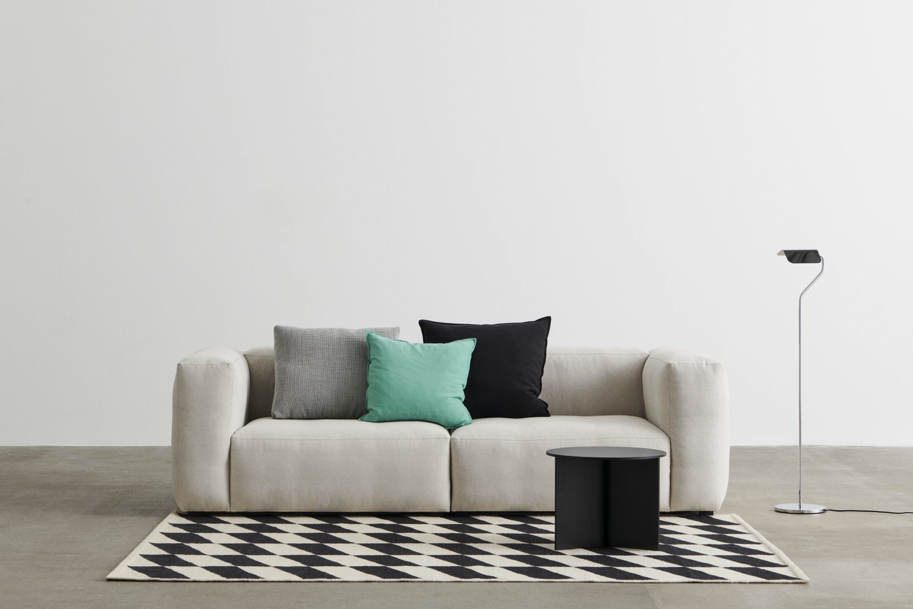 Mags Soft Sofa mit grünen und schwarzen Kissen auf einem schwarz-weiß gemusterten Teppich.