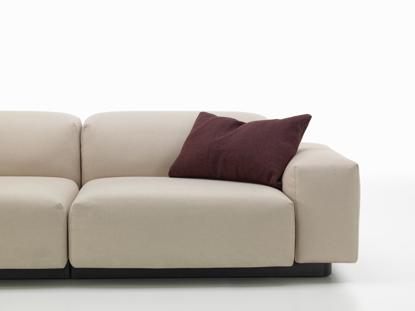 Beige Couch mit einem einzelnen, dunkelroten Vitra Cushions Kissen als Dekoration, modernes Wohnzimmer Design.
