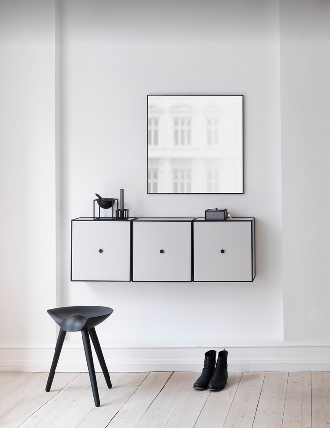 Schwarzer ML42 Hocker von Audo vor weißer Wand mit Schränken und Spiegel im minimalistischen Flur.