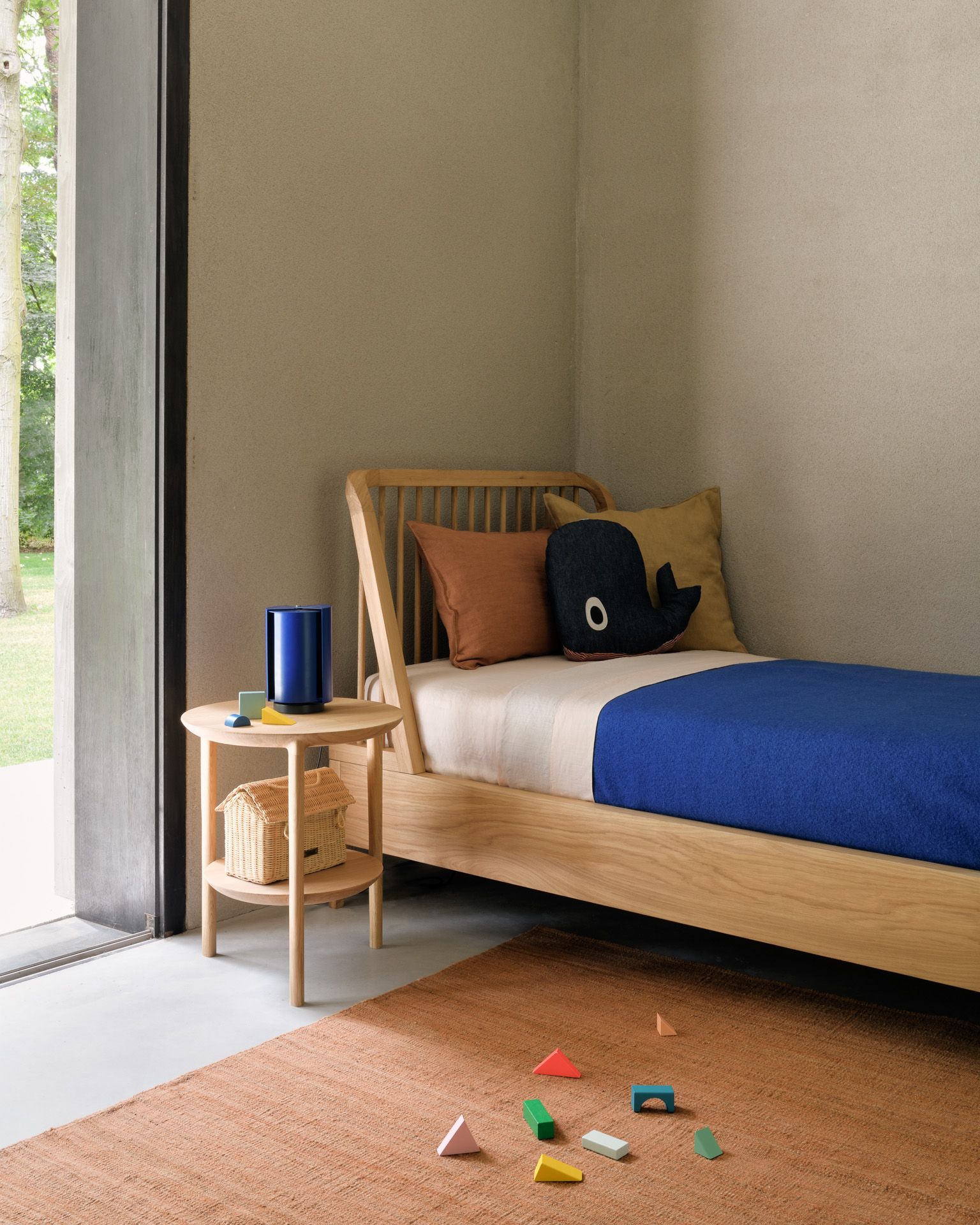 Helles Ethnicraft Spindle Einzelbett aus Holz mit blauer Tagesdecke und Nachttisch im Kinderzimmer.