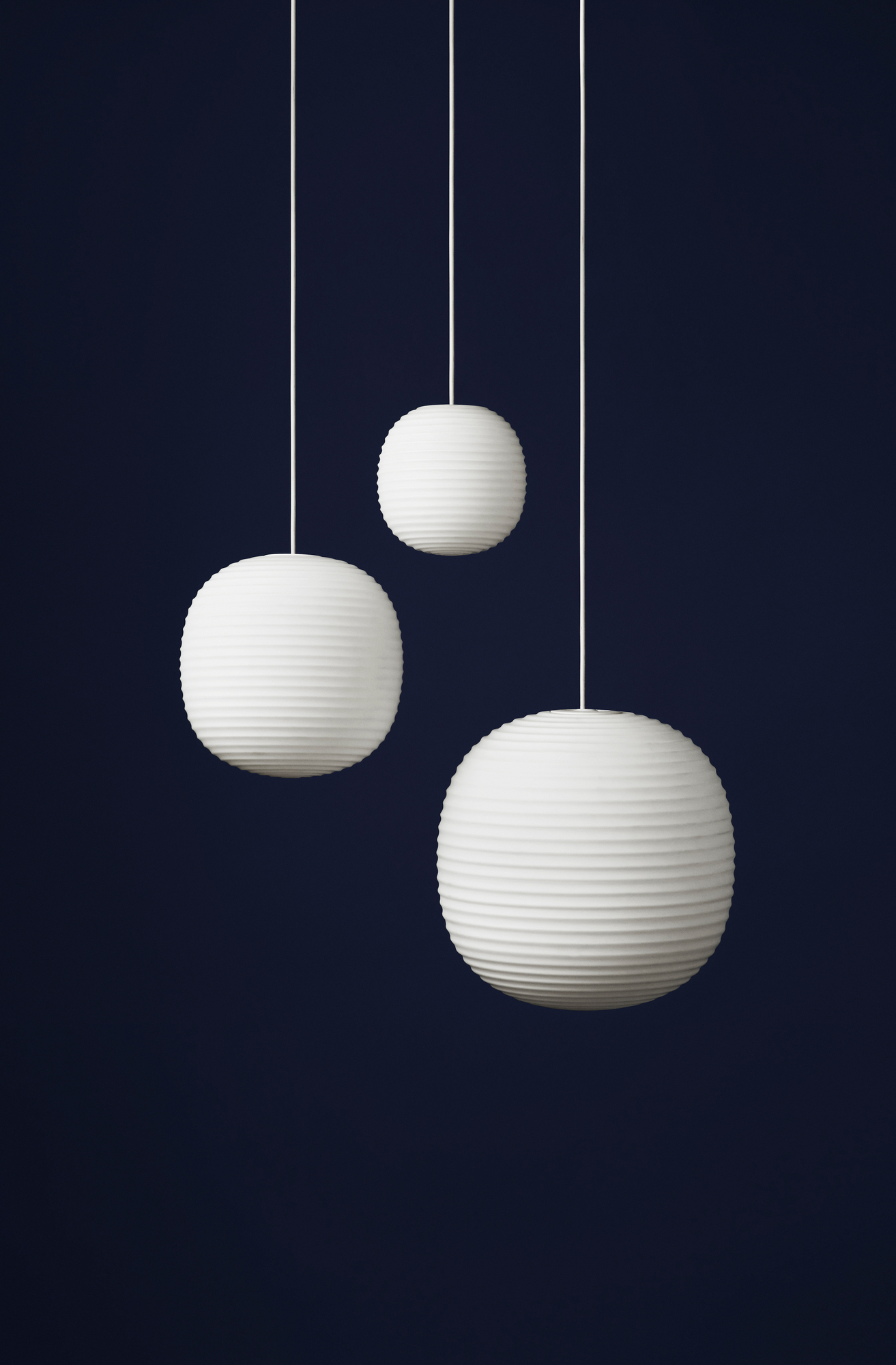 Drei weiße Lantern Pendelleuchten von New Works mit gerippter Oberfläche vor dunklem Hintergrund.