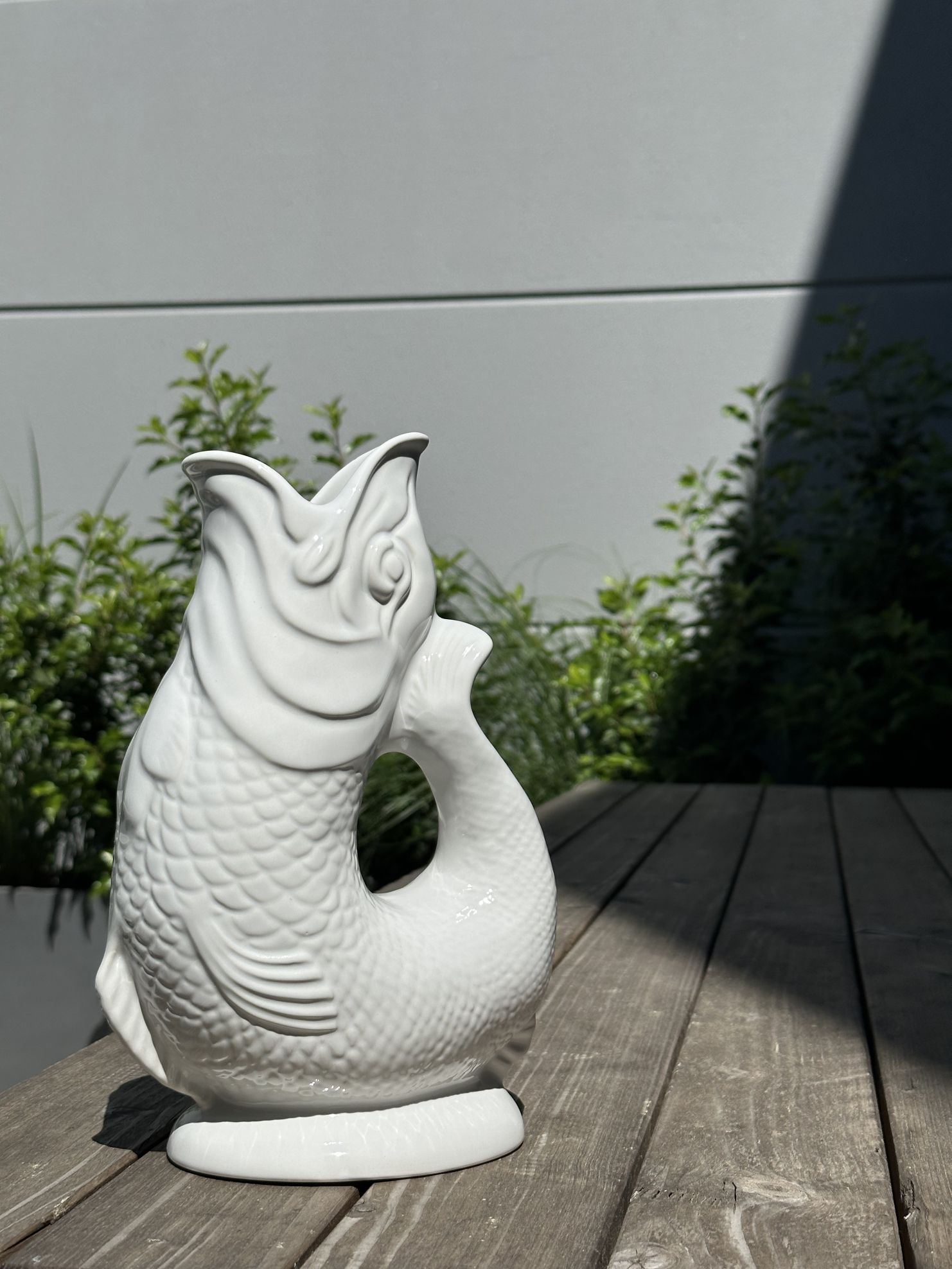 Weiße Gluckigluck Fischkaraffe XL auf Holzterrasse. Dekorative Wasserkaraffe und Vase in Fischform.