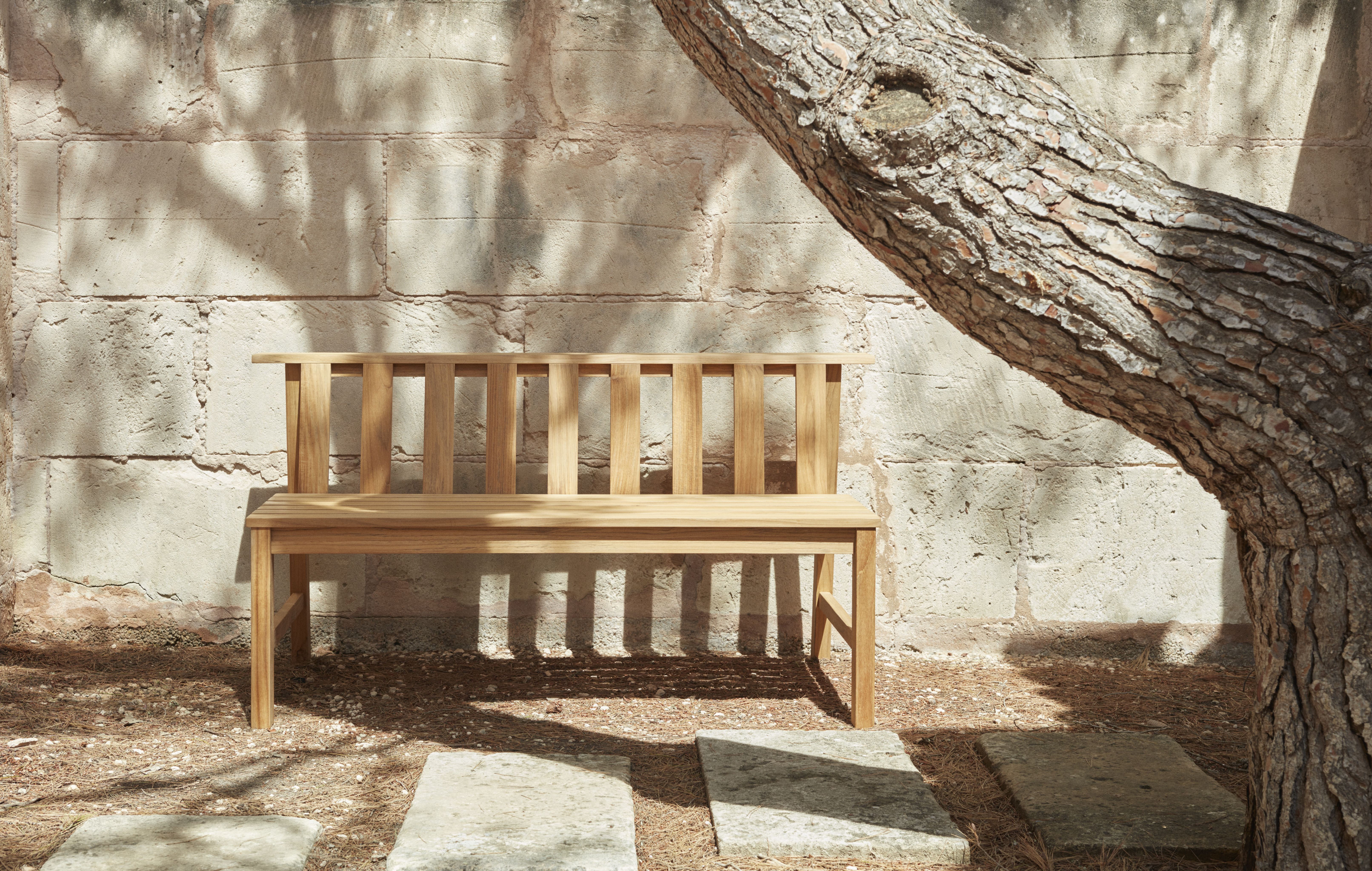 Cadence Bank Teakholz Gartenbank von Skagerak by Fritz Hansen vor einer Steinmauer und Baum.