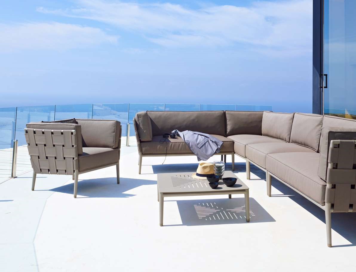 Graue Outdoor Lounge Möbel: Ecksofa, Sessel und Couchtisch auf einer Terrasse mit Meerblick.