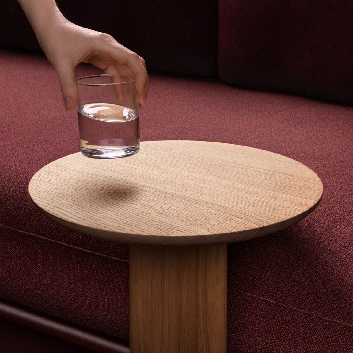 Vitra Anagram Anstecktisch aus Holz, runde Tischplatte, Hand stellt Glas Wasser darauf, modernes Möbeldesign.