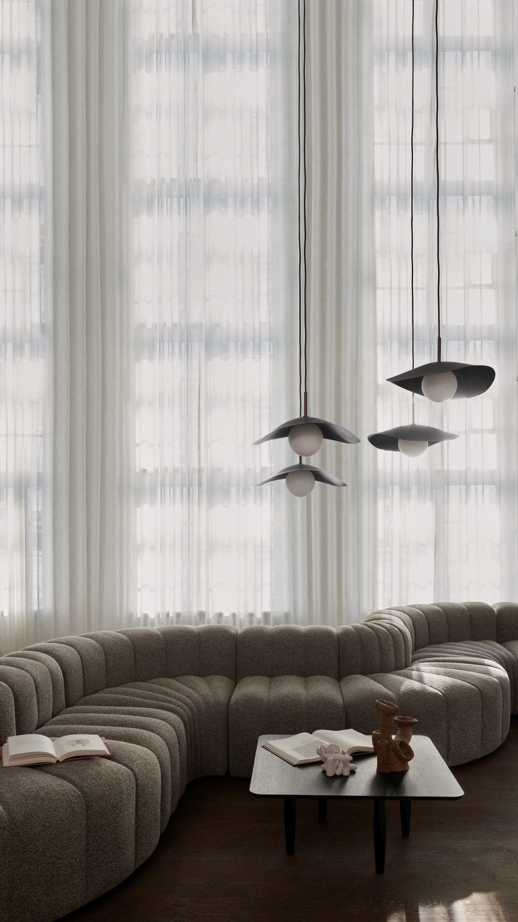Drei graue Fuji Pendelleuchten von Norr11 hängen in einem stilvollen Wohnzimmer mit Sofa.