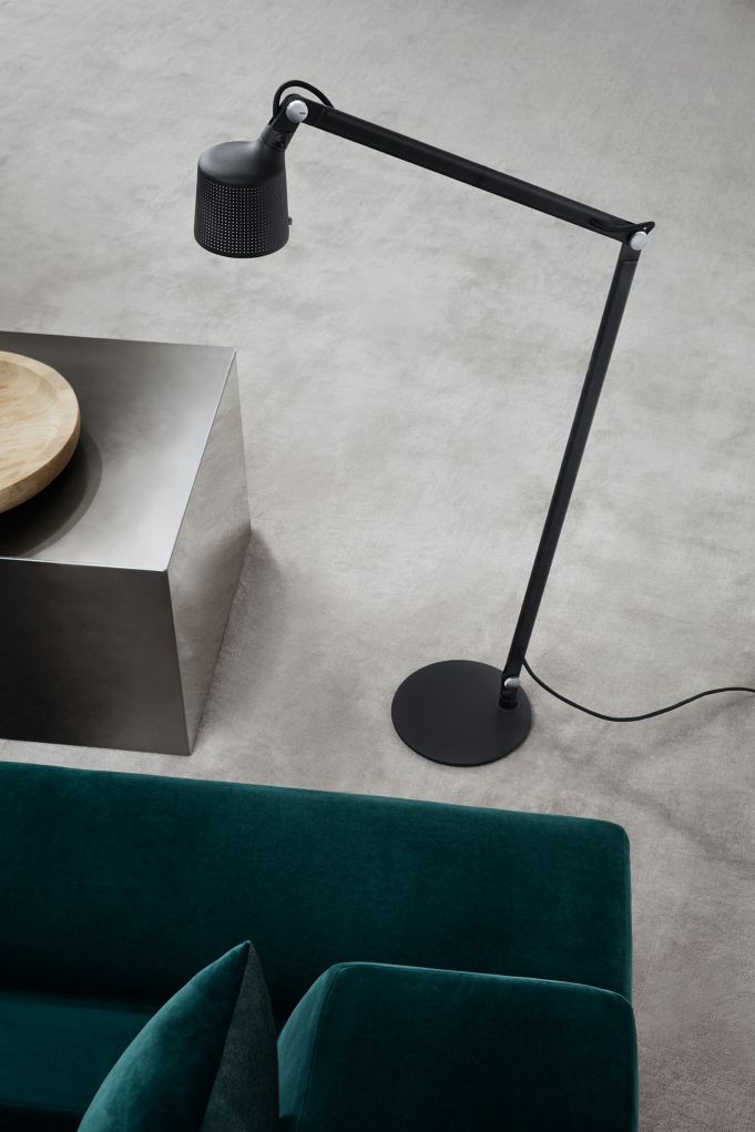 Schwarze Vipp Boden Leselampe mit verstellbarem Arm und perforiertem Lampenschirm neben Sofa und Beistelltisch.