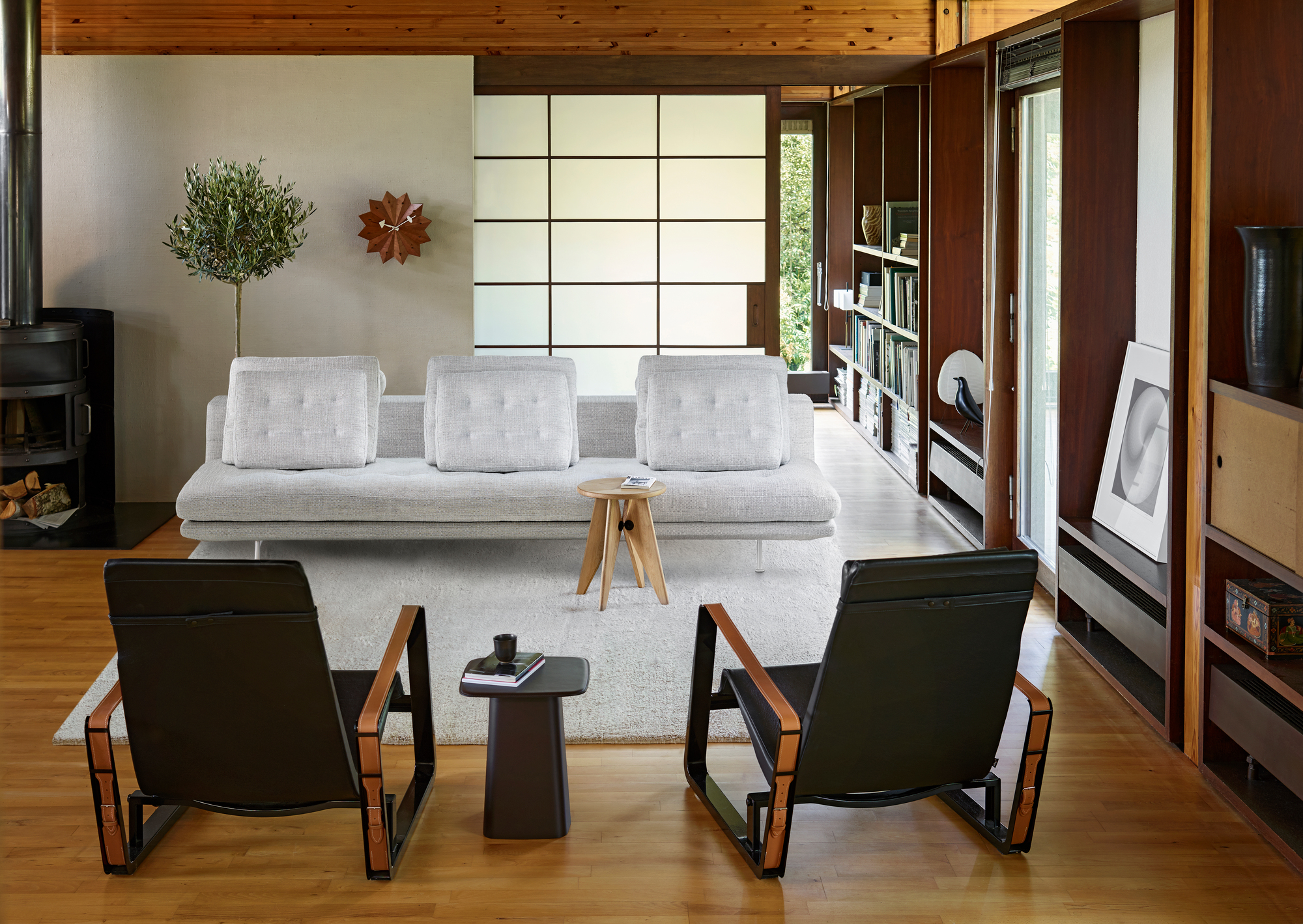 Helles Wohnzimmer mit Vitra Grand Sofa 3,5-Sitzer in Grau, zwei schwarzen Sesseln und Holzelementen.