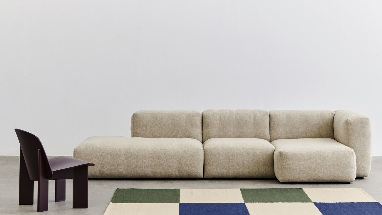Beiger Chisel Lounge Chair Sessel von Hay neben modularem Sofa und Teppich mit Schachbrettmuster.