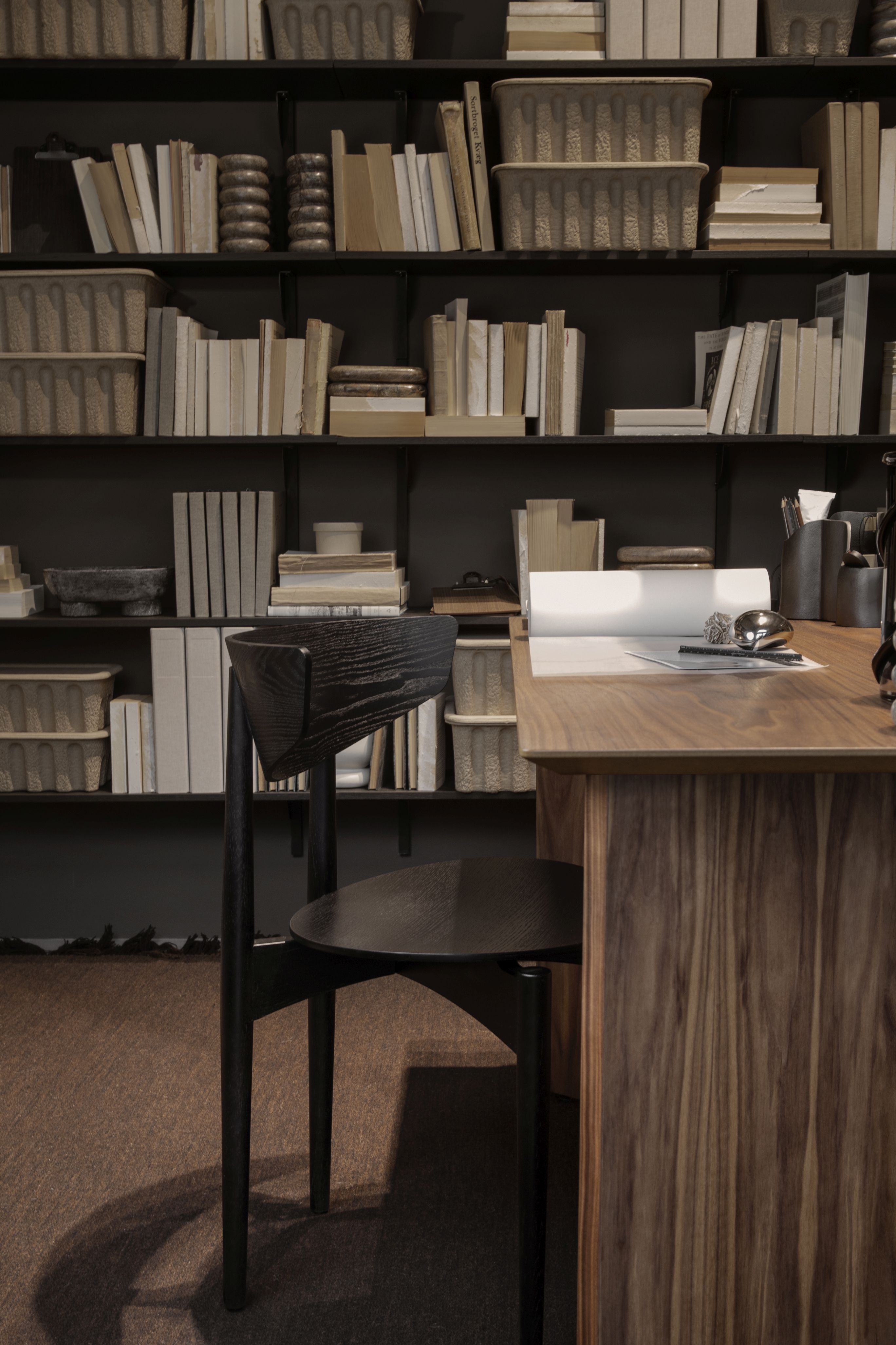 Schwarzer Herman Esszimmerstuhl von Ferm Living mit Holzgestell vor Bücherregal und Schreibtisch.