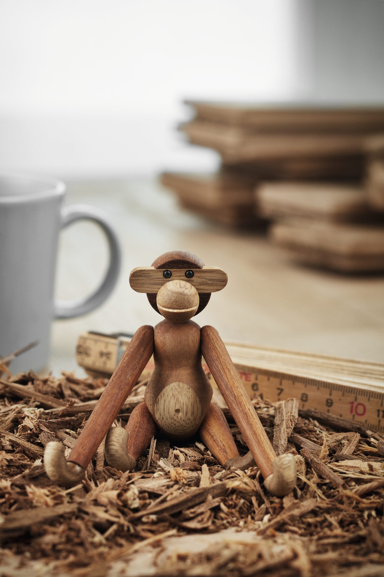 Affe Mini Holzfigur Teak Kay Bojesen sitzend auf Holzspänen, daneben Zollstock und Tasse.