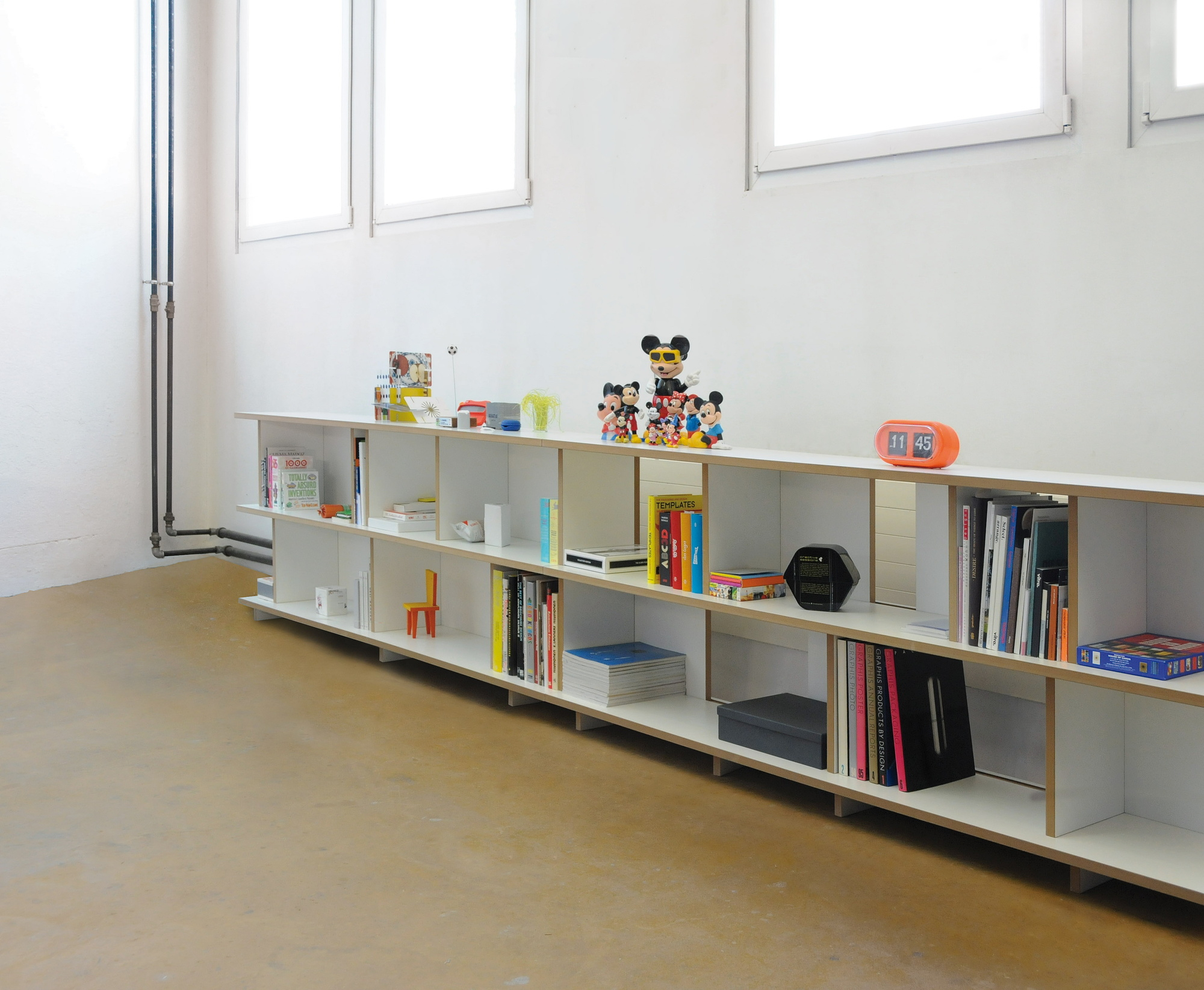 Weißes Tojo Stell Regal Grundmodul mit Büchern und Dekorationen vor einer weißen Wand.