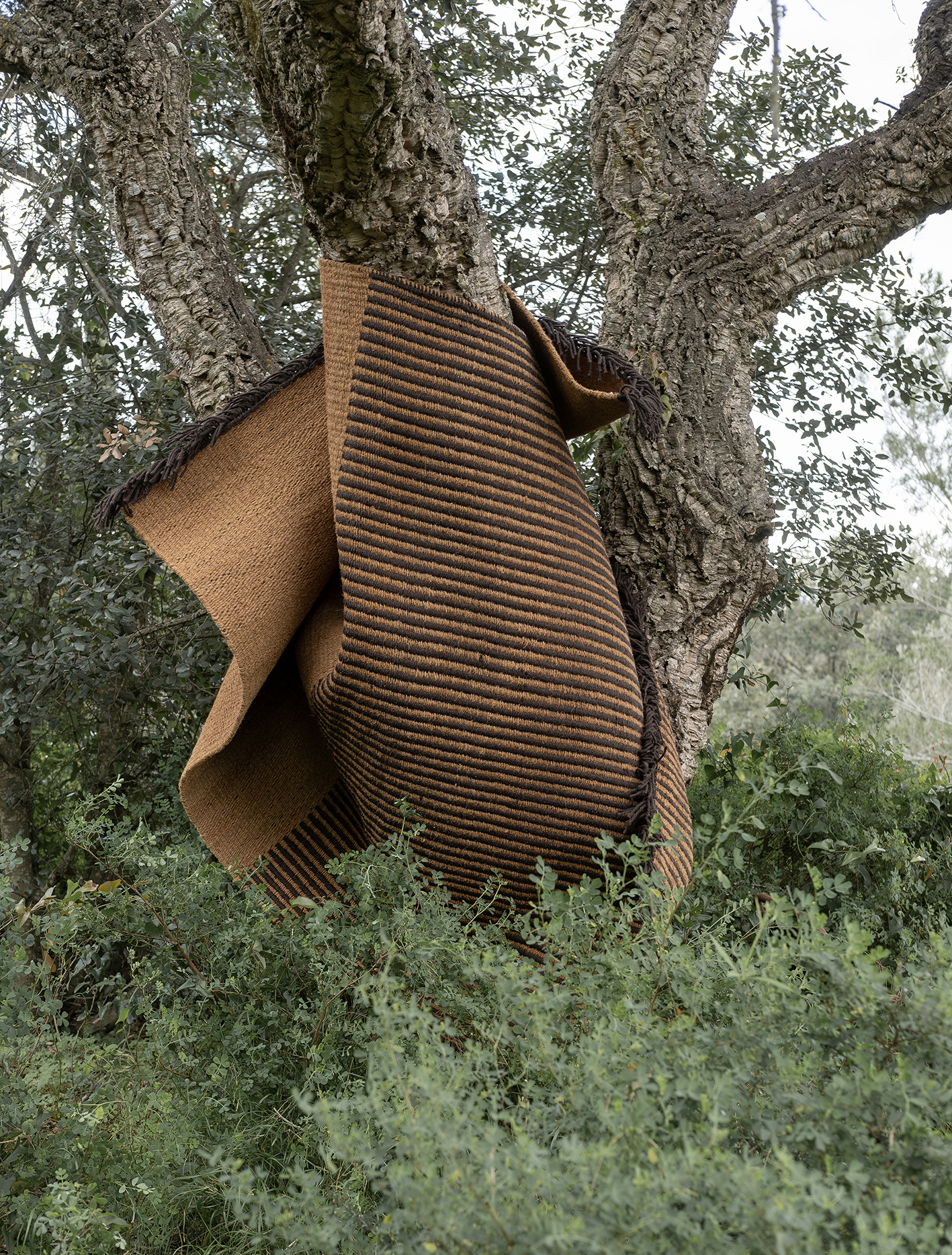 Nanimarquina Outdoor Teppich, braun gestreift, an einem Baum hängend, ideal für Garten und Terrasse.