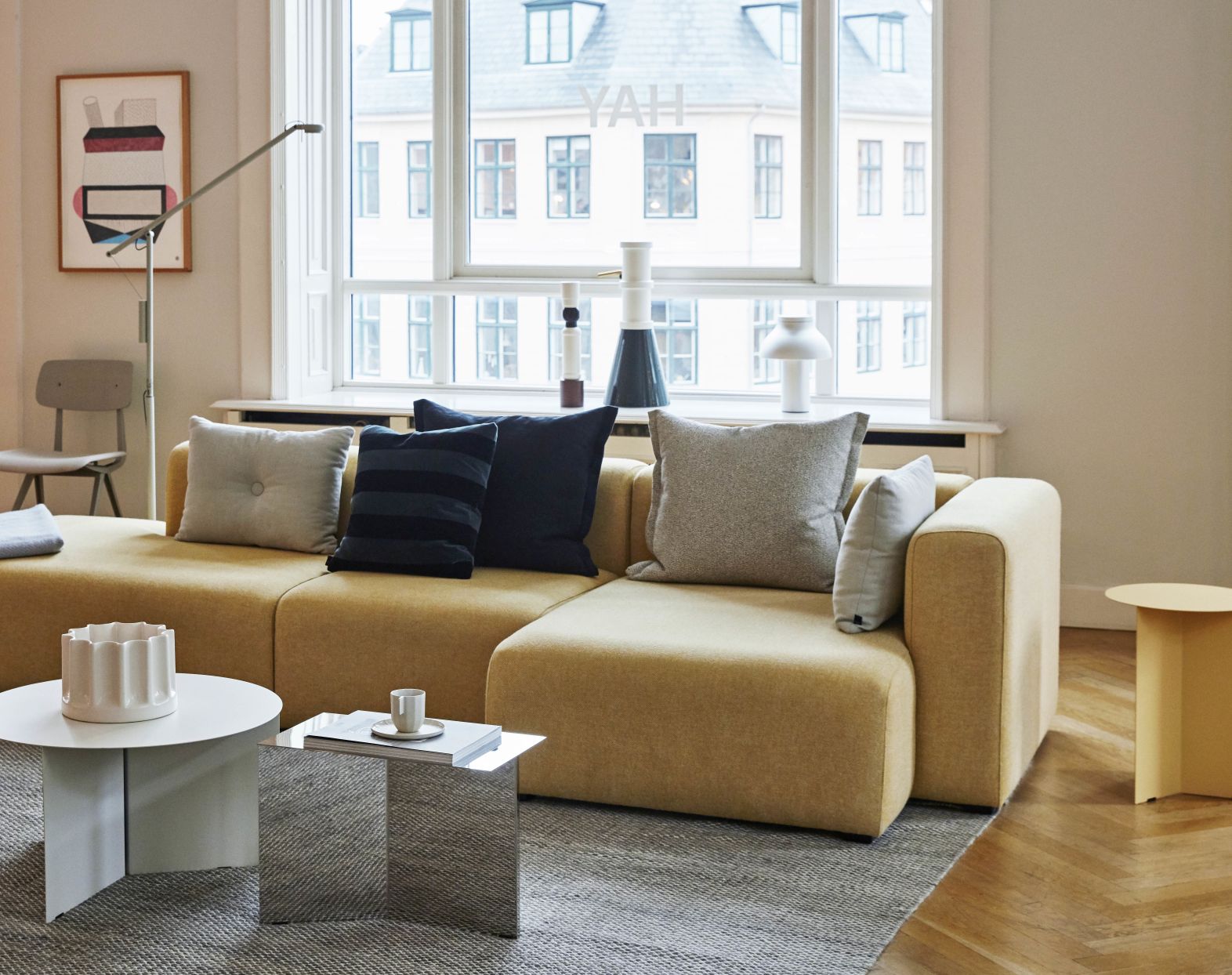 Wohnzimmer-Szene mit Hay Slit Table Beistelltisch, oblong, spiegelpoliert, neben gelbem Sofa auf grauem Teppich.