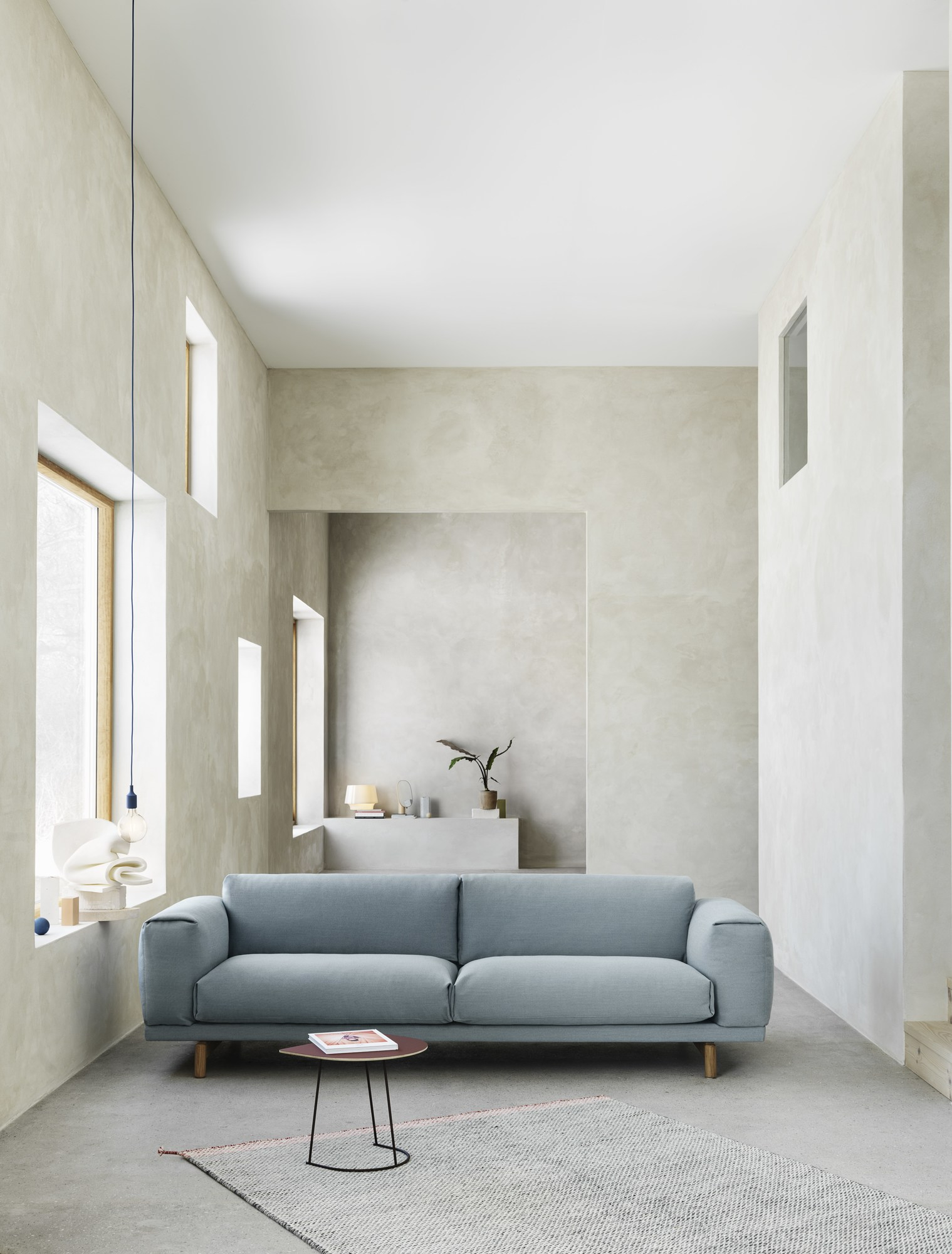 Helles Wohnzimmer mit blauem Muuto Rest Sofa, kleinem Tisch und minimalistischer Dekoration.