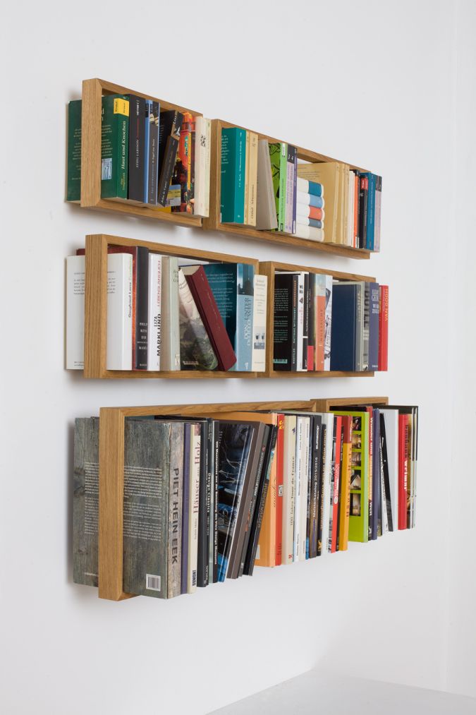 Drei schwebende, minimalistische Regal b Eiche Regale an einer weißen Wand, gefüllt mit Büchern.