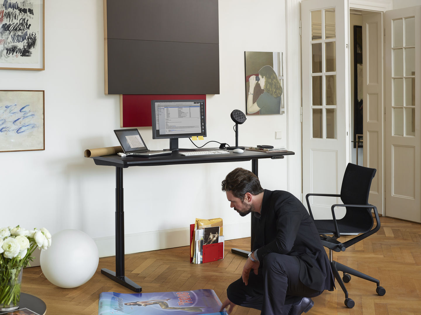Schwarzer Physix Bürodrehstuhl von Vitra neben höhenverstellbarem Schreibtisch in modernem Büro mit Mann.