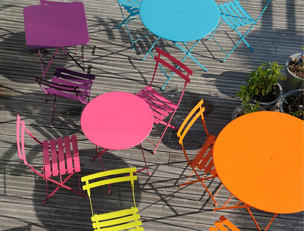 Farbige Fermob Bistro Gartentische und Stühle aus Metall auf einer Holzterrasse, ideal für den Außenbereich.