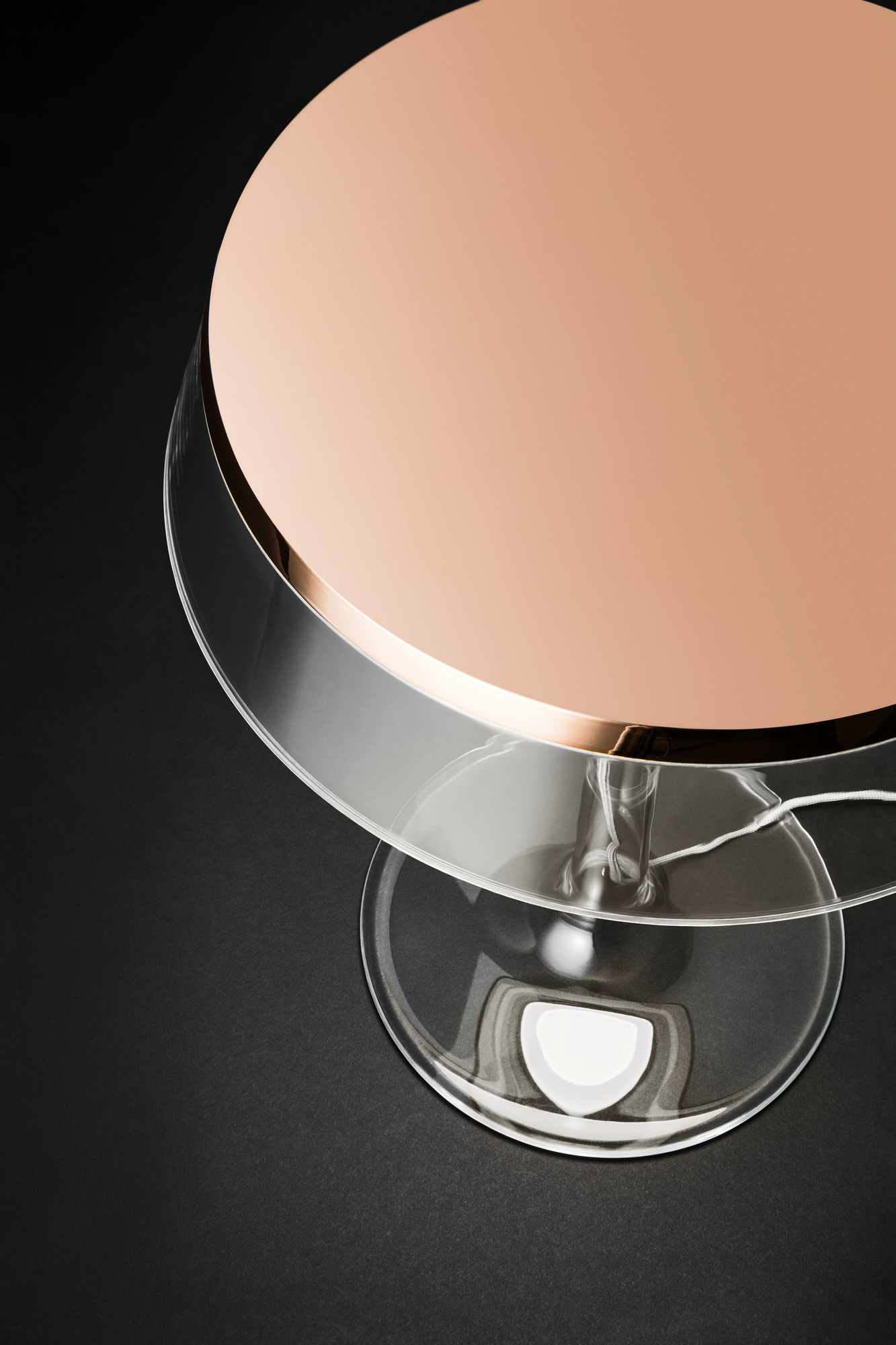 Detailaufnahme der Bon Jour Tischleuchte von Flos mit roségoldenem Schirm und transparentem Fuß auf schwarzem Hintergrund.