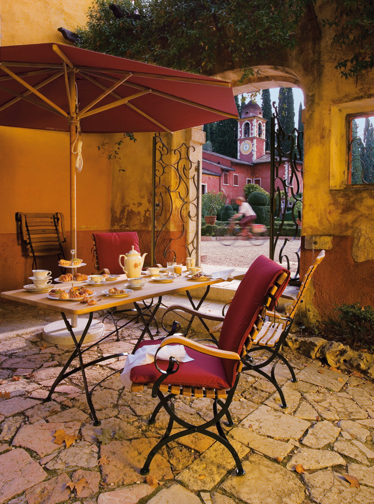 Weishäupl Classic Armchair Sessel klappbar mit Armlehnen auf sonniger Terrasse mit Frühstückstisch und Sonnenschirm.