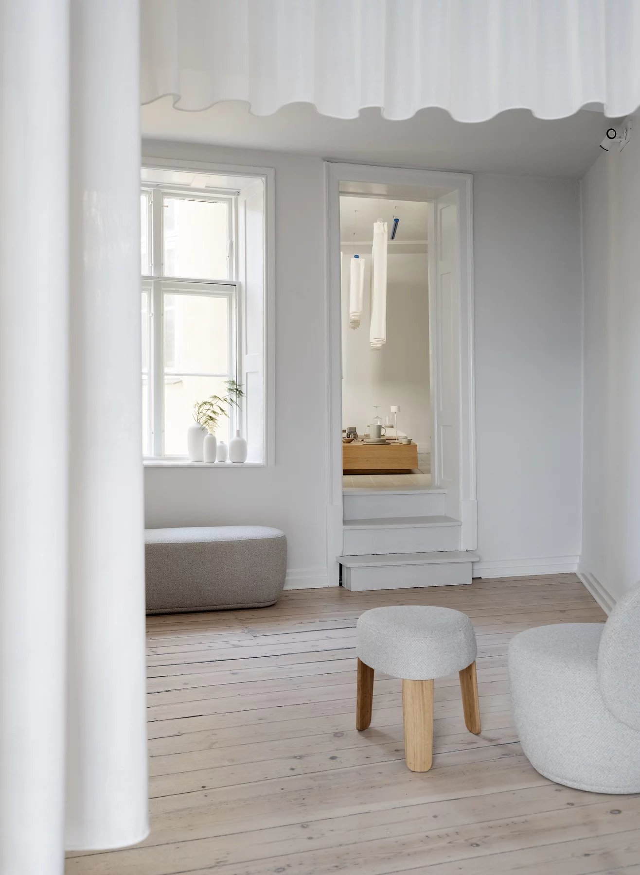 Helles Wohnzimmer mit Blomus Socia Möbeln: Hocker, Bank und Teilansicht eines taupefarbenen Sofas.