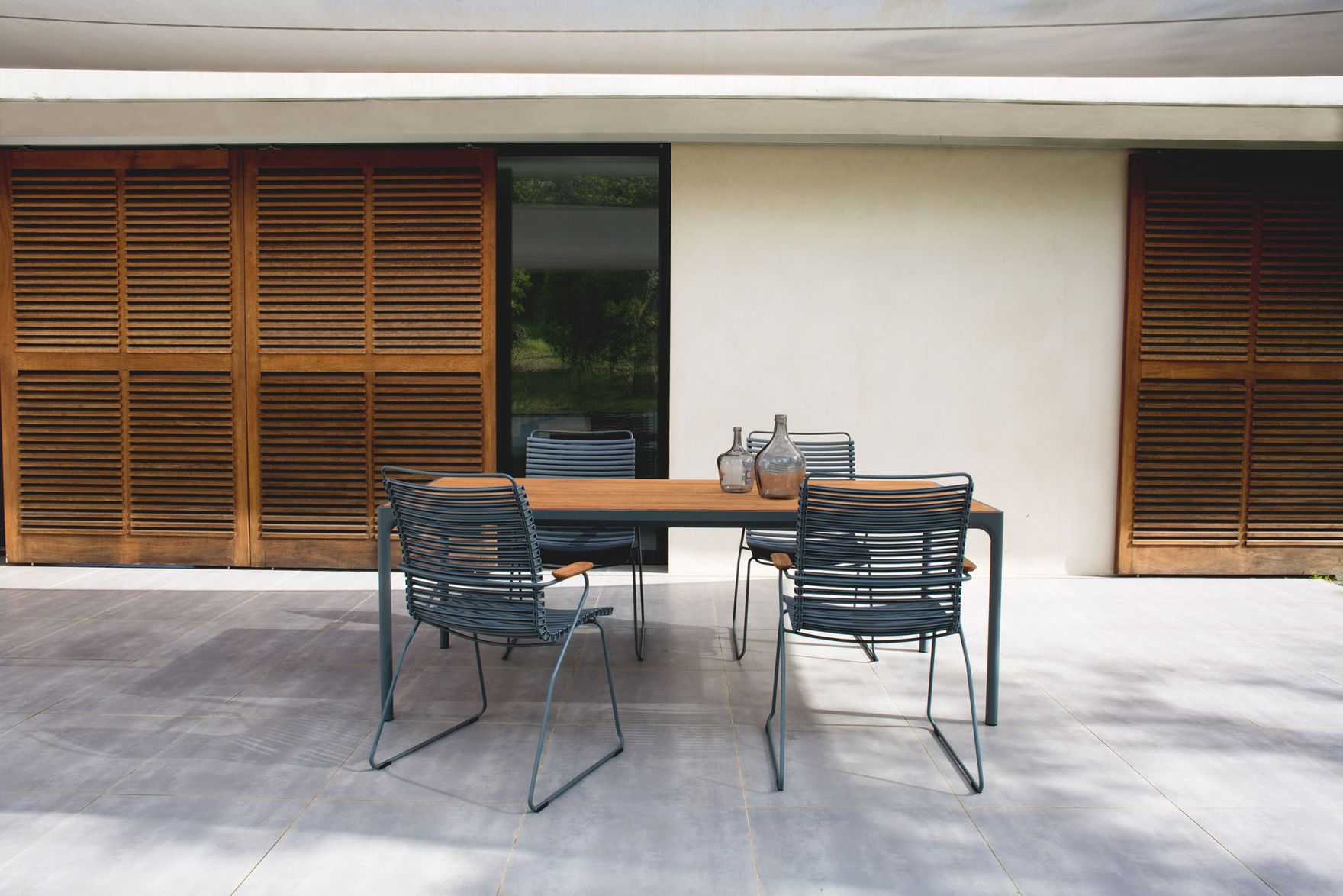 Dunkelgraue Click Lounge Sessel von Houe Outdoor mit Holztisch und Glasflaschen auf einer Terrasse.